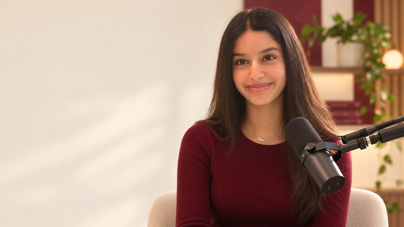 Reva Desai wearing burgundy at a black podcast microphone